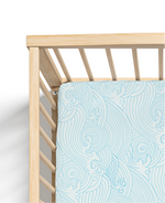 A fitted crib sheet with a blue wave pattern, made from a blend of bamboo and organic cotton muslin, designed to fit a standard crib mattress.