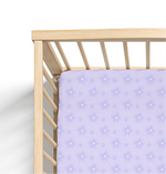 A purple crib sheet with a daisy pattern fitted on a crib with wooden rails.
