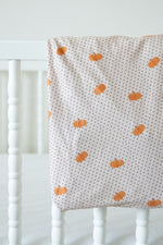 Crib sheet with pumpkin pattern draped over a white crib