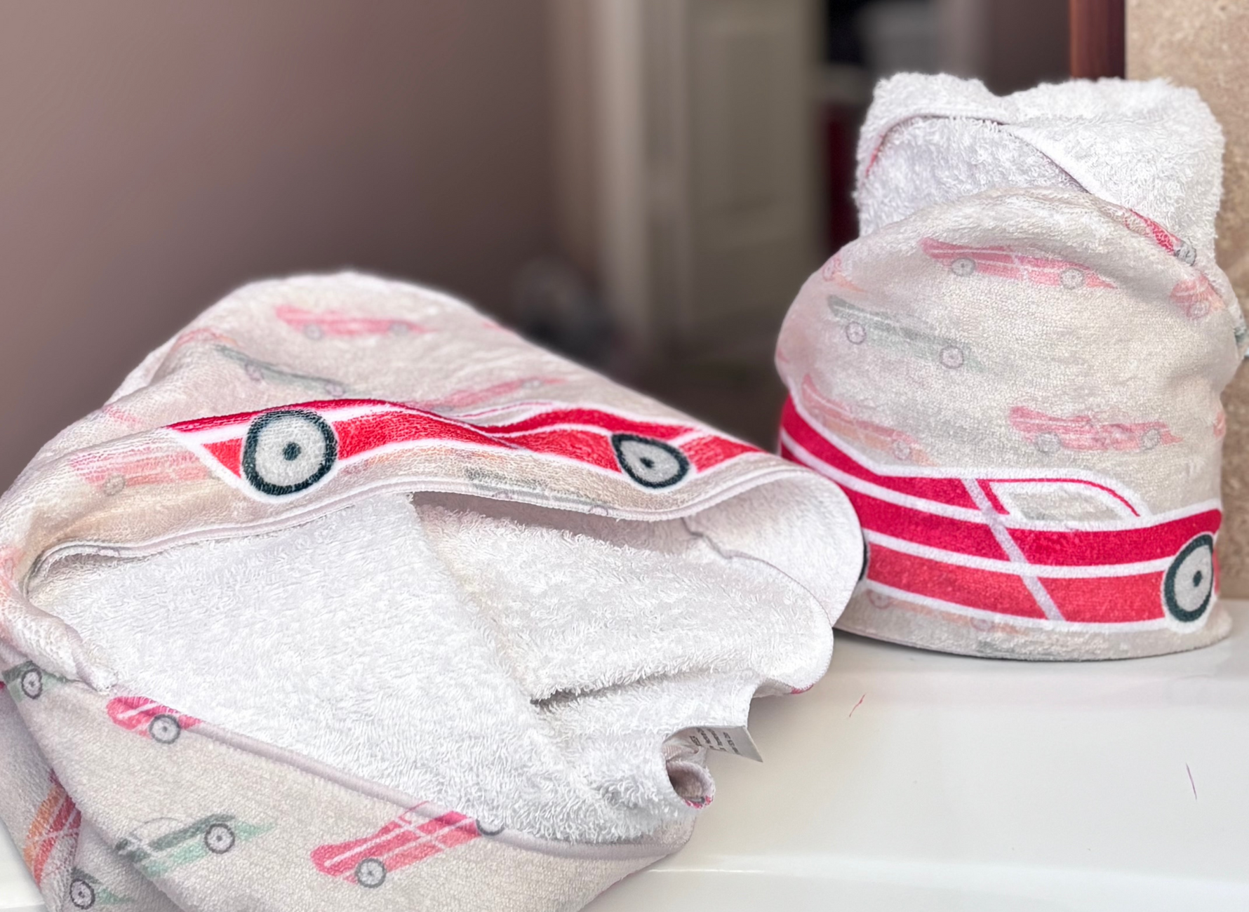 race car baby hooded towel featuring multi-colored racecars as a pattern on pastel khaki background color - features a bright red 'toy car' styled race car