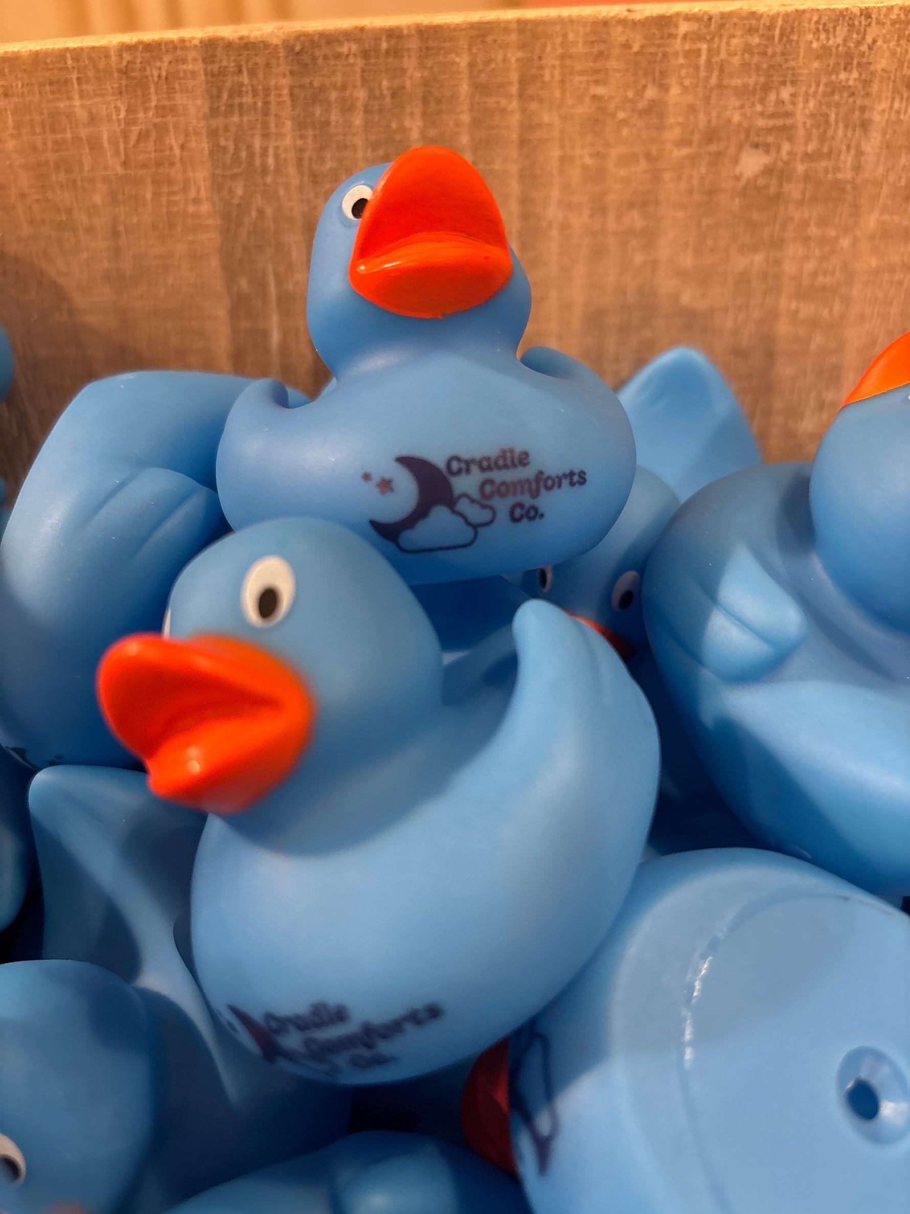 A pile of blue rubber ducks with red beaks, branded with 'Cradle Comforts Co.'