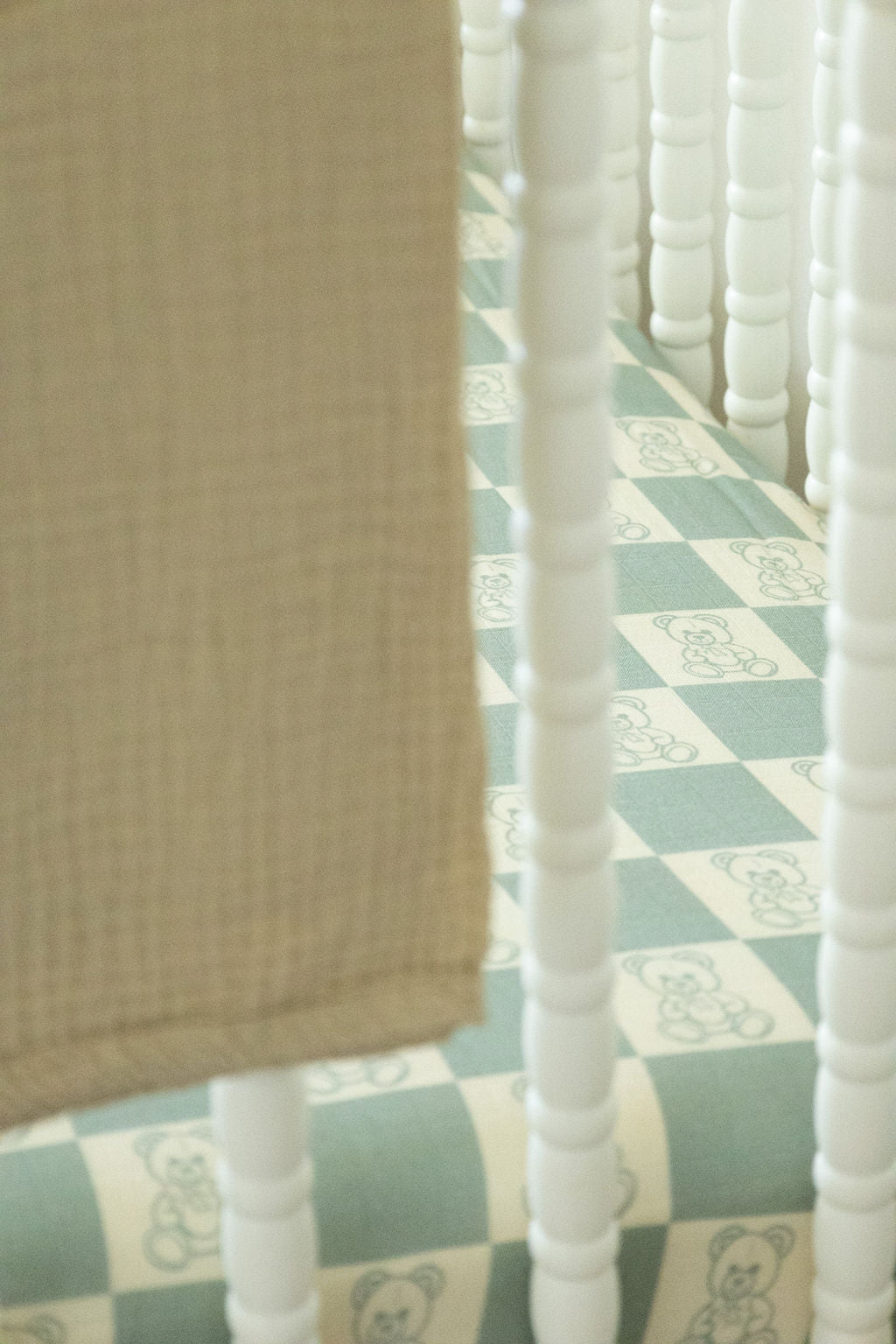 Close-up of a crib with a checkered sheet and teddy bear pattern