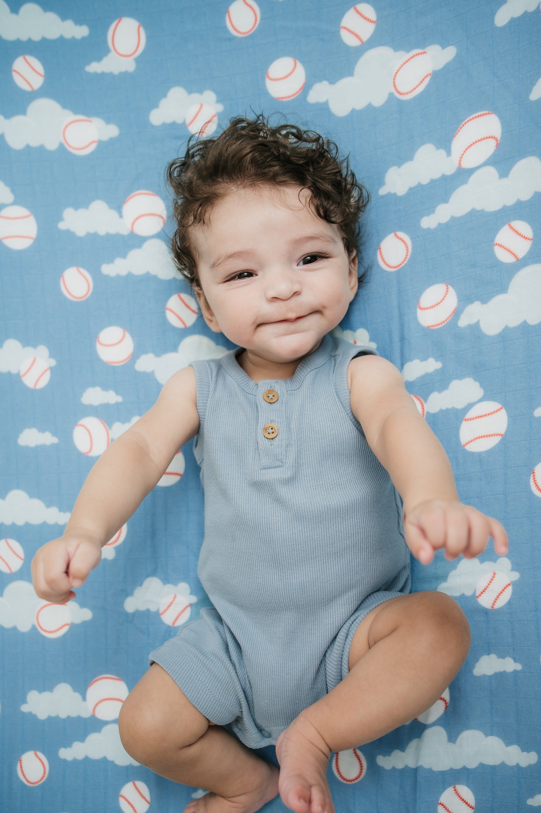 Baby lying on a blue blanket with cloud and baseball pattern