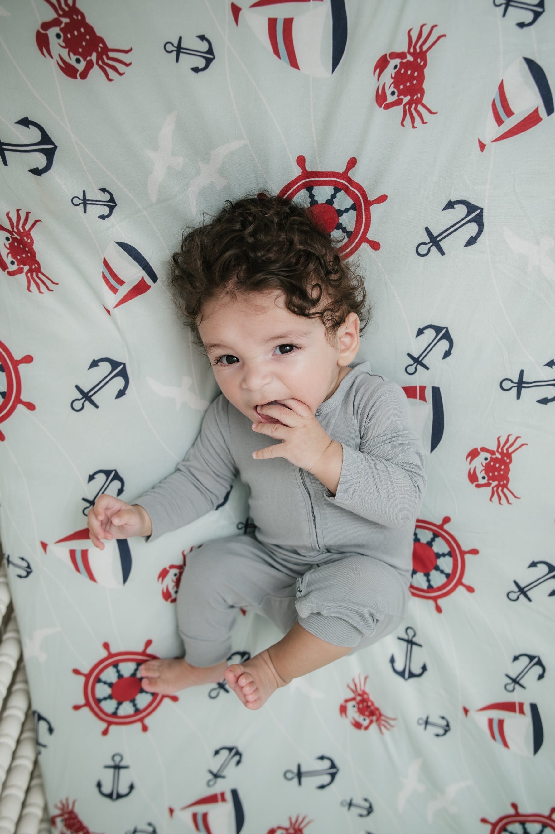 Child lying on a crib with a nautical patterned sheet