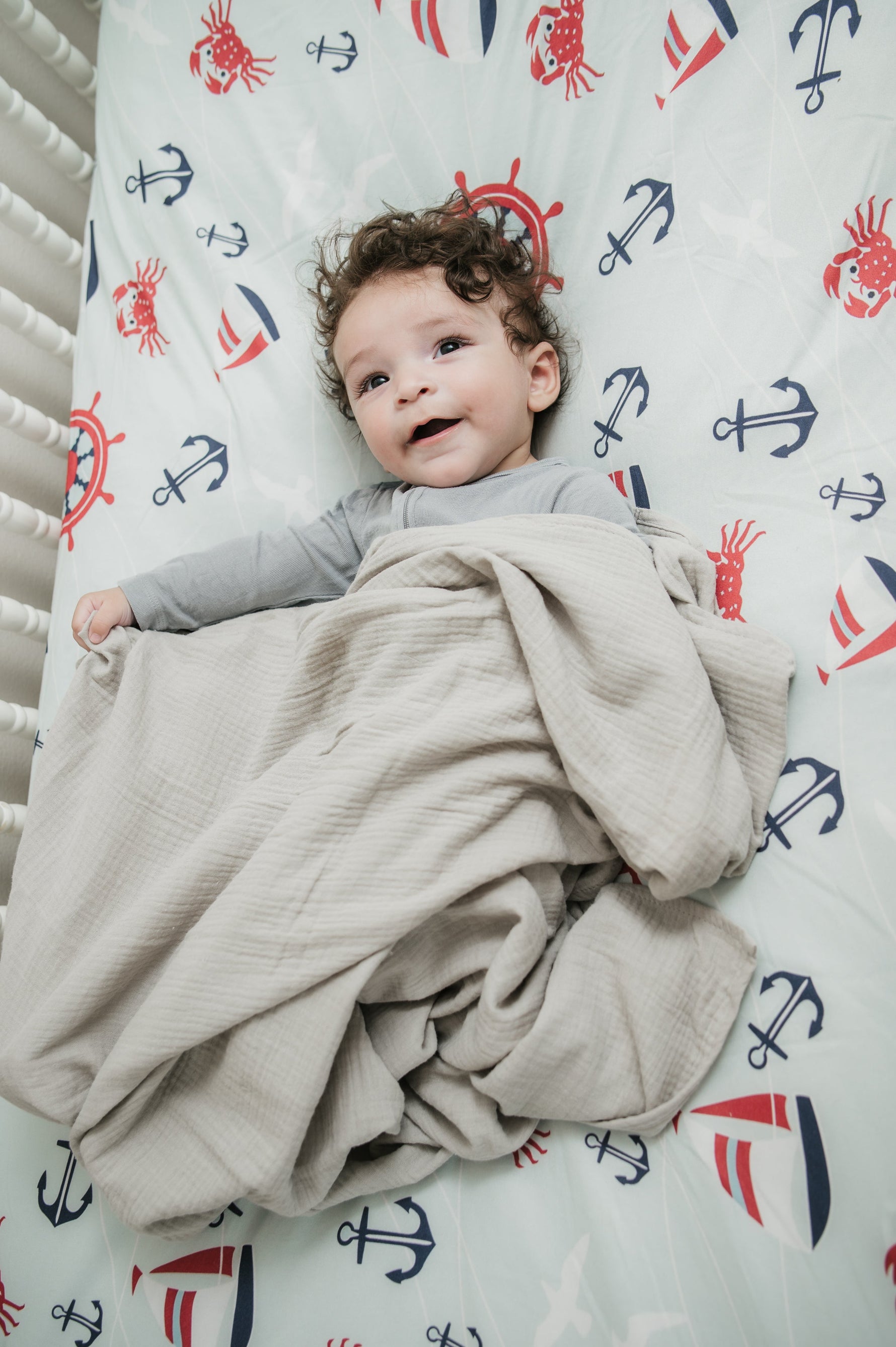 Baby wrapped in a beige blanket on a crib with nautical-themed bedding