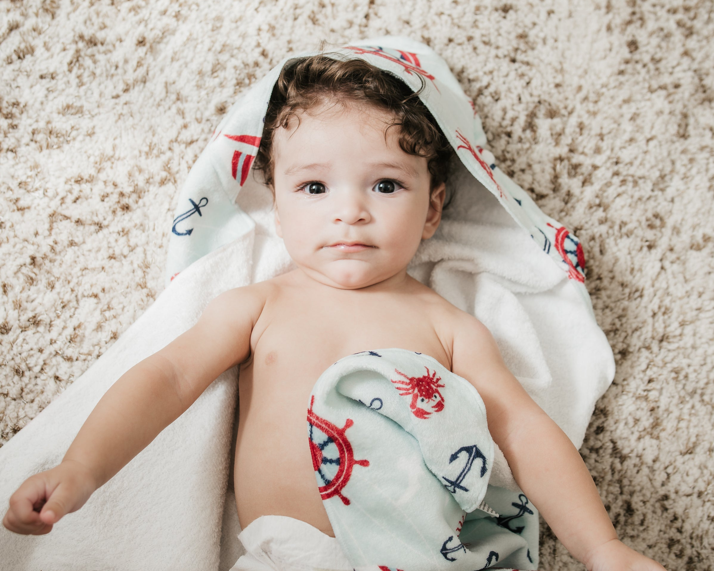 Baby wrapped in a towel with a pattern on a carpeted floor