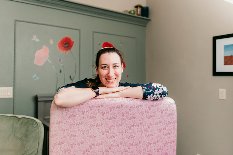 founder of cradle comforts co. leaning on crib sheet with butterflies on it