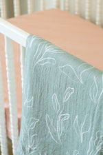 Light green textured blanket with white leaf patterns draped over a crib.