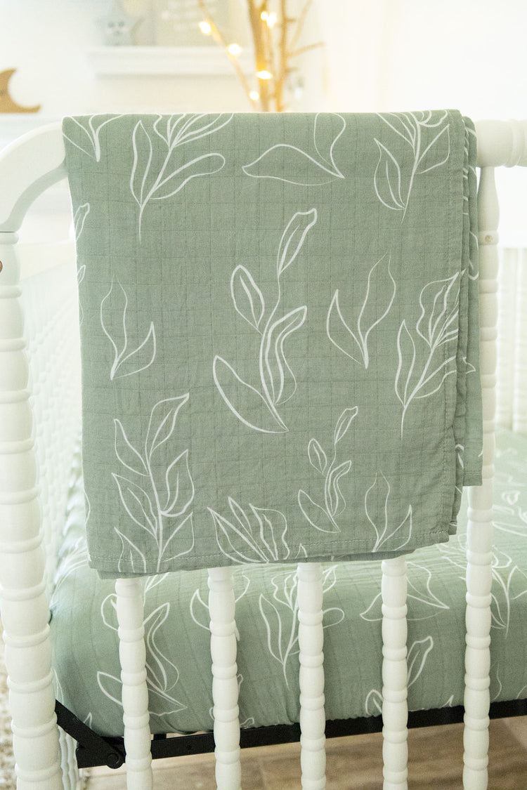 Green leaf-patterned blanket draped over a white crib