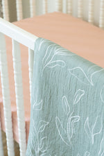 Green textured blanket with white leaf patterns draped over a crib.