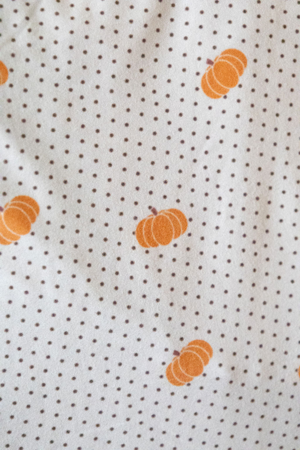 Fabric with small orange pumpkins on a tan background with dark brown polka dots